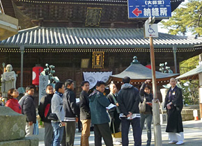 Participants receive an explanation from an executive monk in front of the main hall of Zentsuji Temple.
